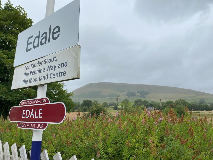 Edale railway station sign with Peak District fell in the background on a cloudy day