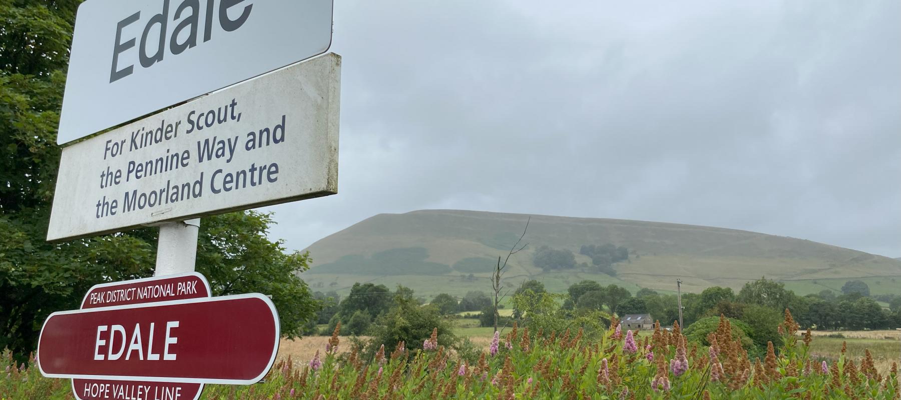 Edale railway station sign with Peak District fell in the background on a cloudy day