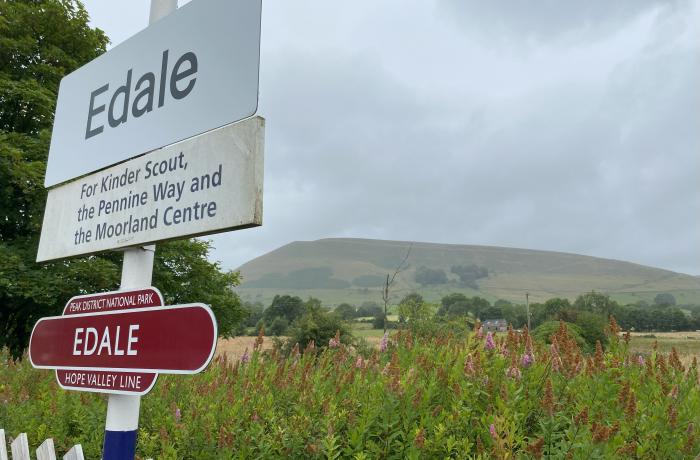 Edale railway station sign with Peak District fell in the background on a cloudy day