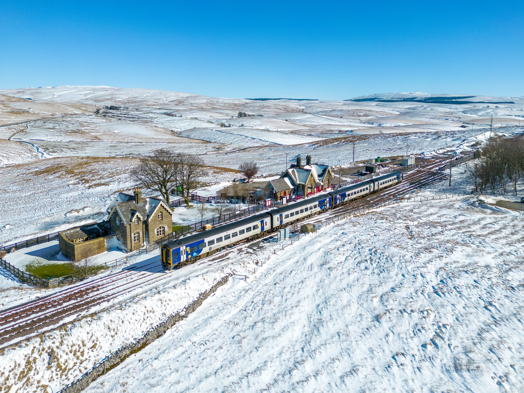 View of Ribblehead station from above with Northern train and snowy landscape