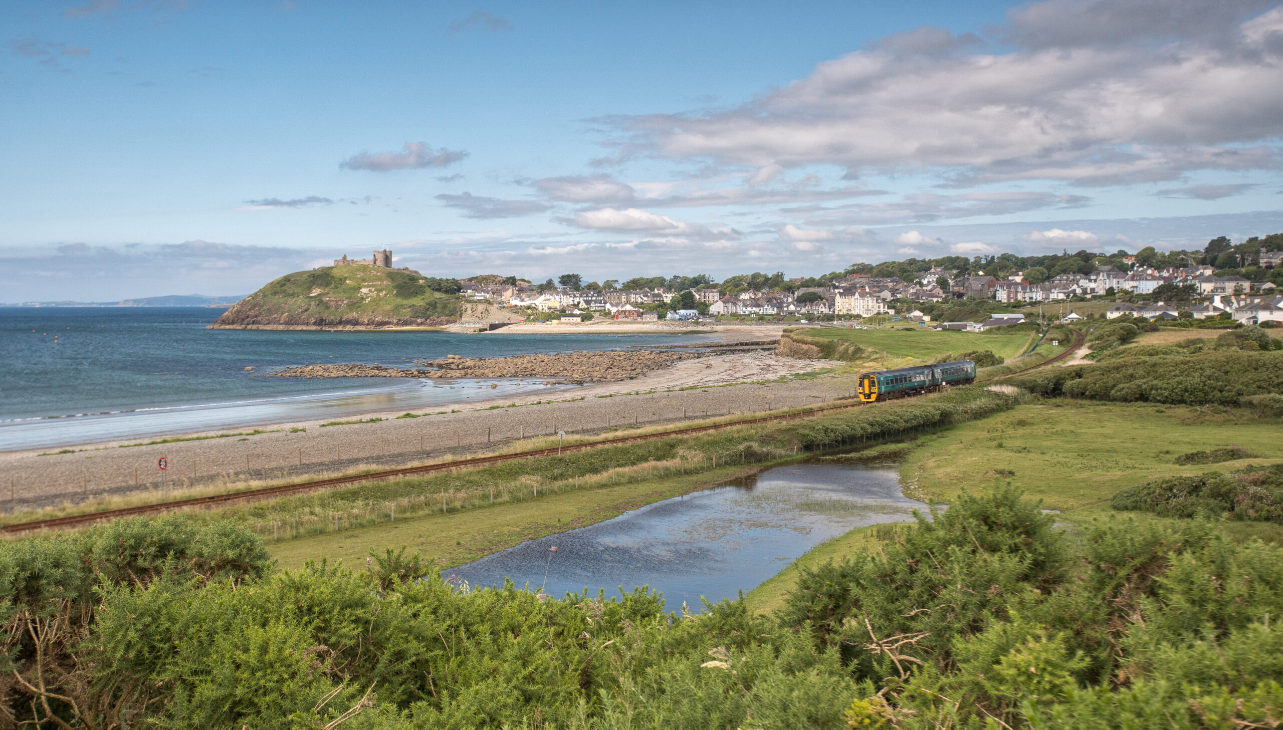 Cambrian Coast Line train travelling by the Welsh Coast with castle and village in background