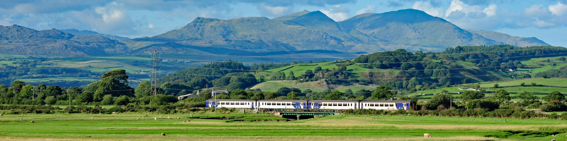 Train travelling past lush countryside with Lake District fells in the background