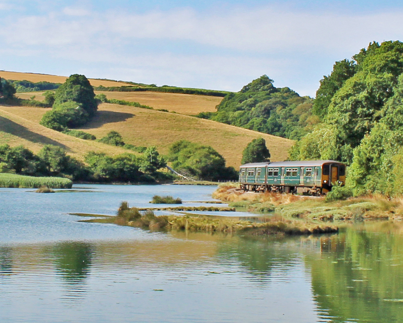 Train travelling along the Looe Valley Line with water and rolling fields either side