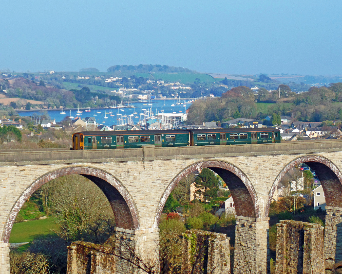 Train travelling over viaduct with sailboats in background