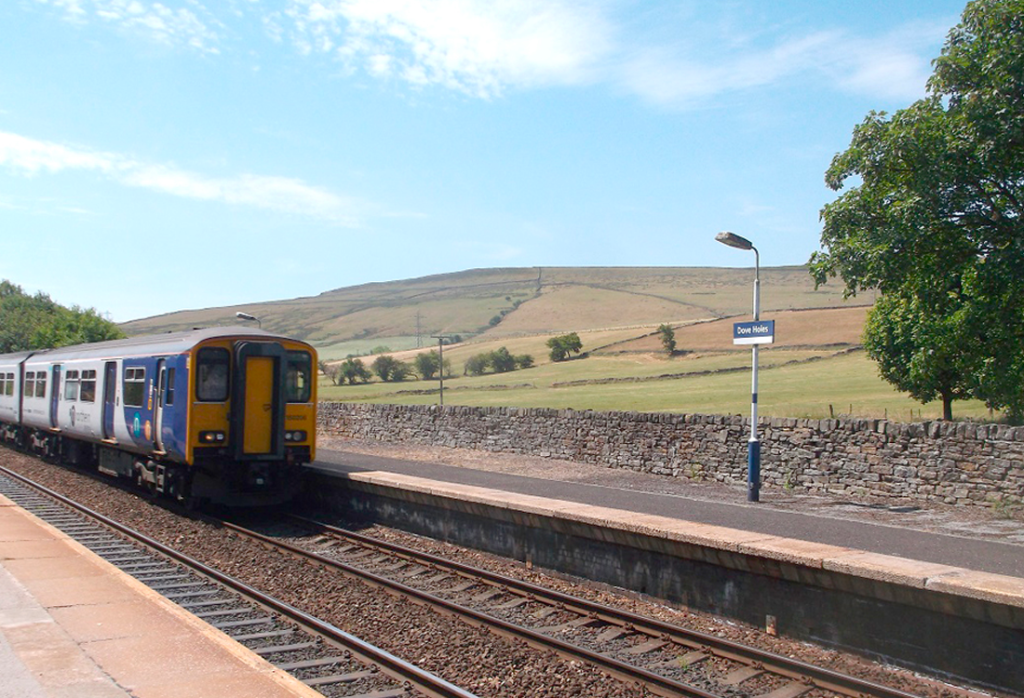 Train approaching Dove Holes along the Buxton Line with rolling Peak District hills in the background on a blue sky day out