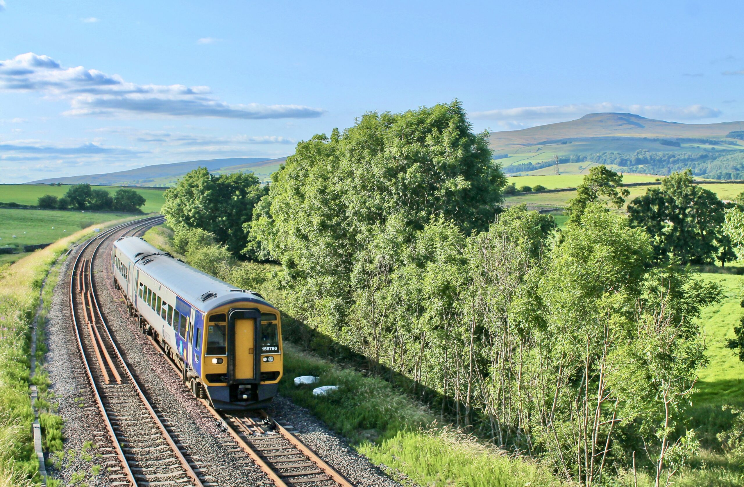 Train travelling past luch green countryside on a sunny day along The Bentham Line