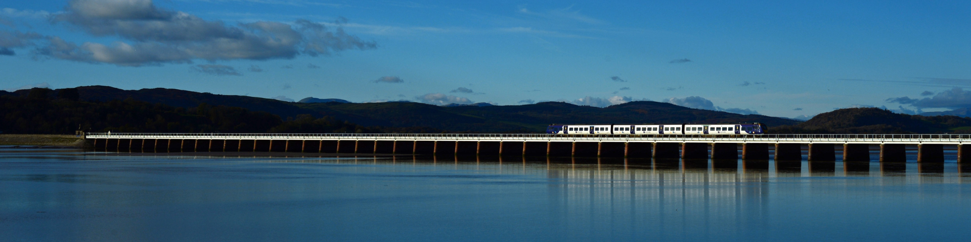 Train journeying along viaduct on Furness Line with Lake District fells in background