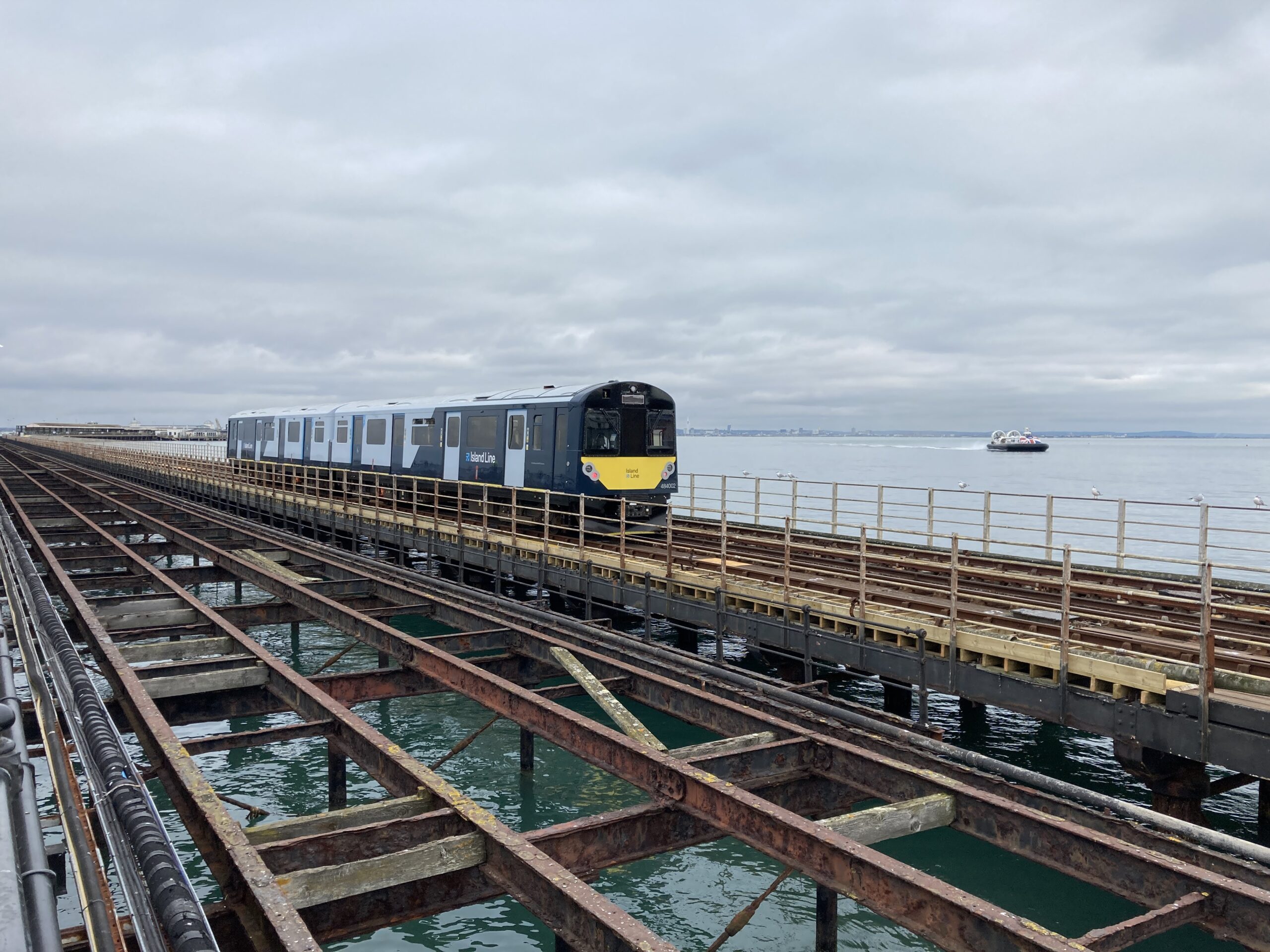 Train travelling along pier with sea and hovercraft in background