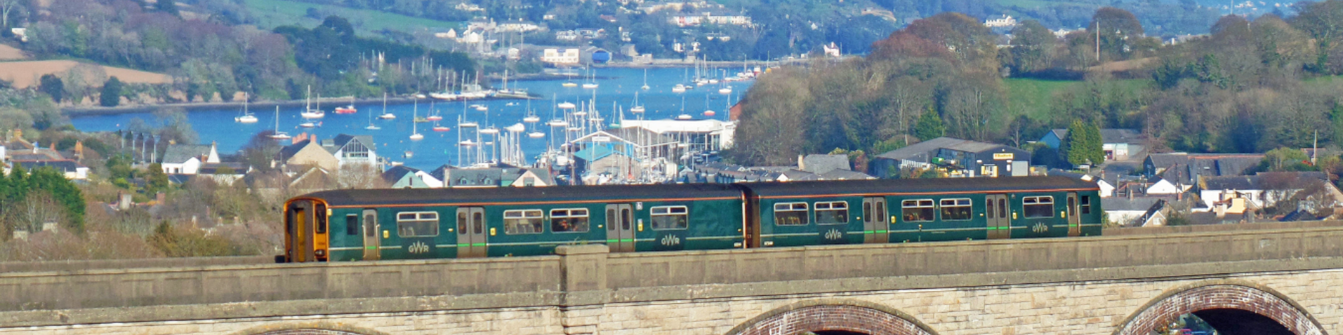 Train travelling over viaduct with sailboats in background