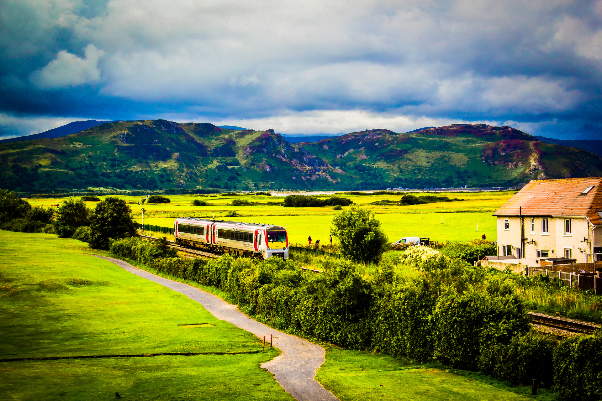 Single house at the side of railway tracks with mountain in background and train travelling past.