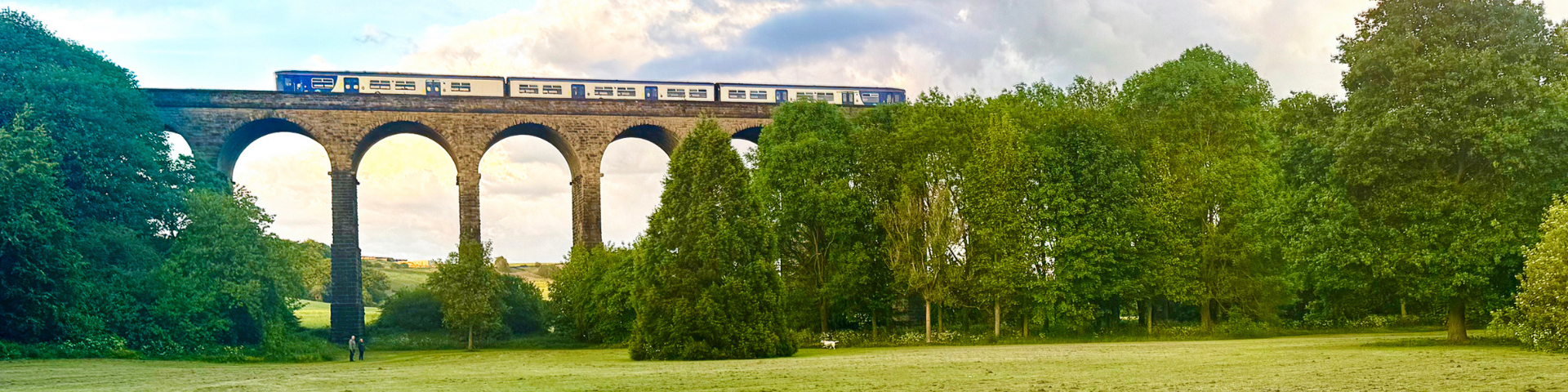 Train travelling across Penistone Viaduct with lush green trees and countryside surrounding.