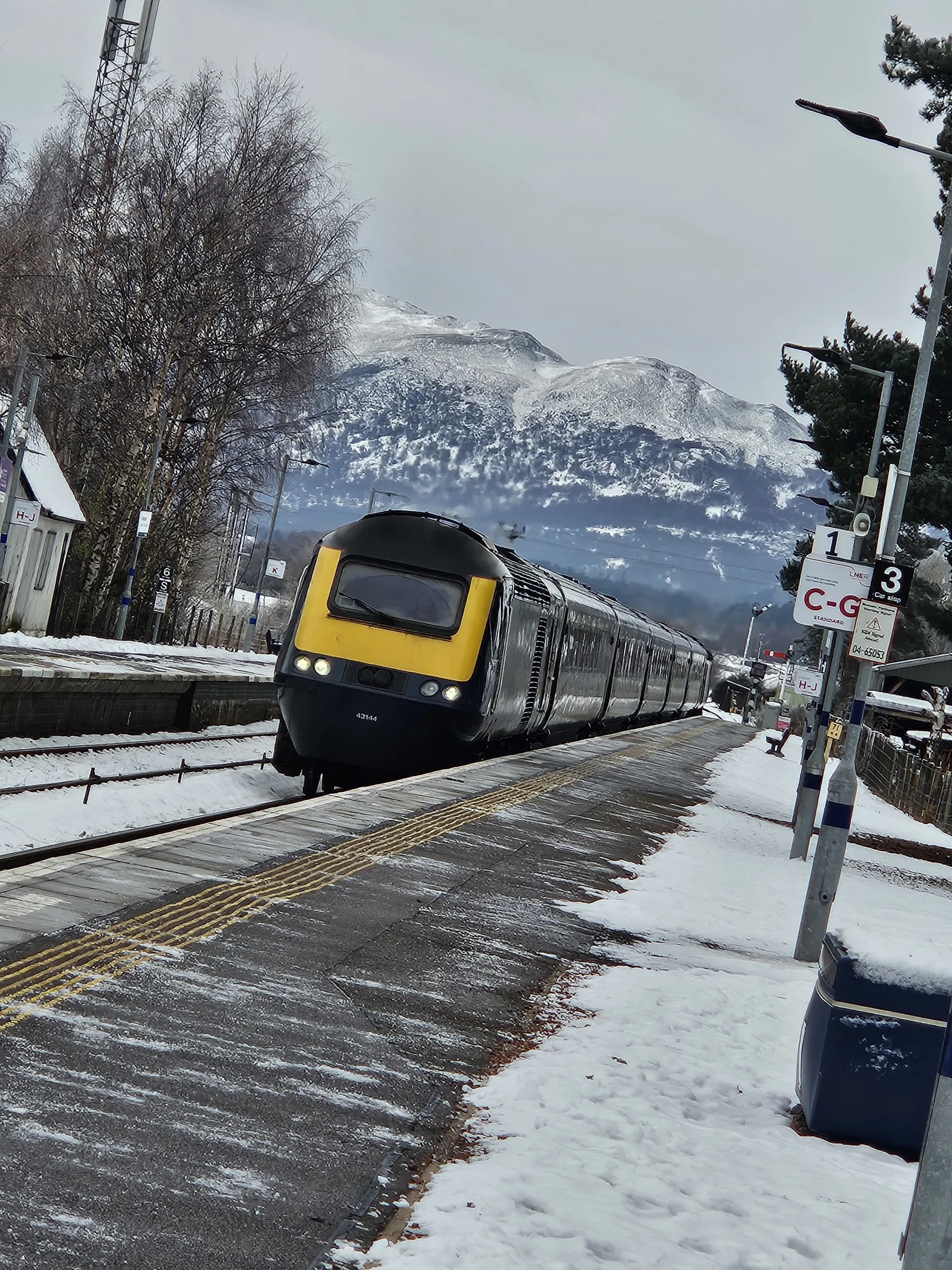 Train at Kingussie Railway Station along the Highland Main Line with snowy mountains in the background | Scenic Rail in Winter