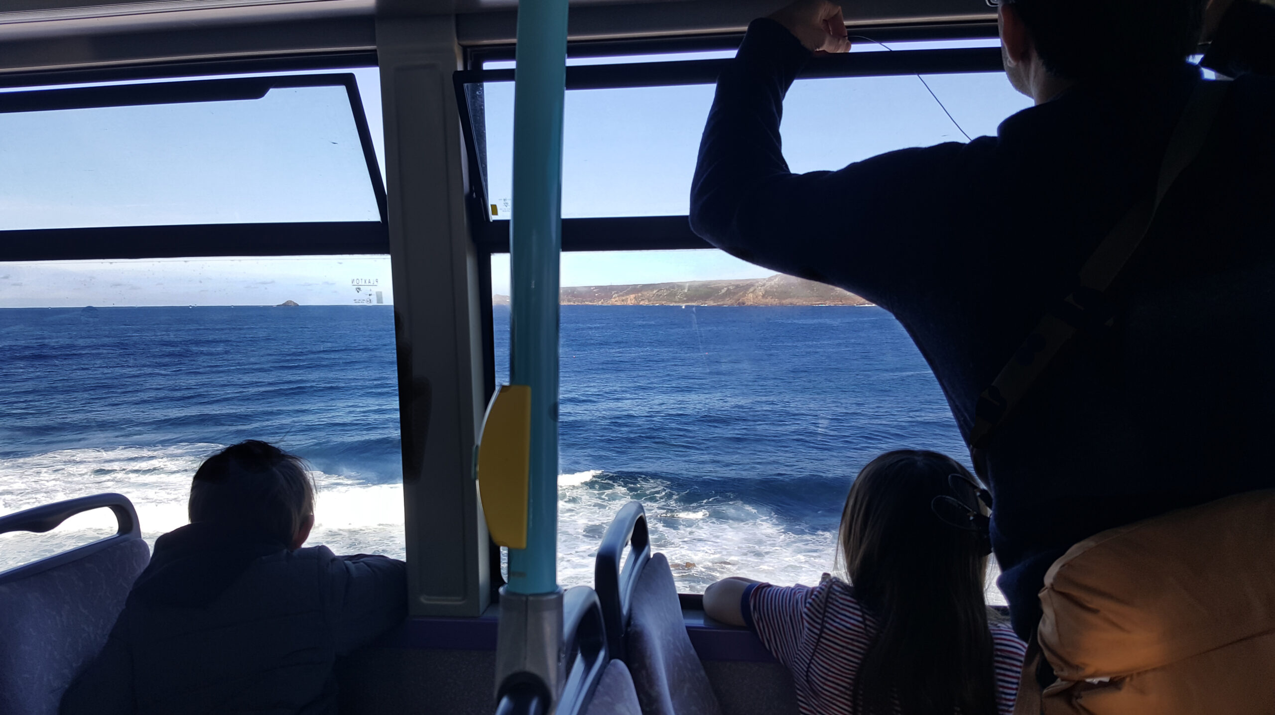 People looking out of the bus window at the crashing waves and blue sky