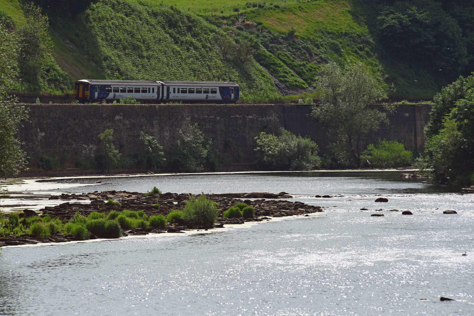 Northern train travelling by the side of water along the Tyne Valley Line