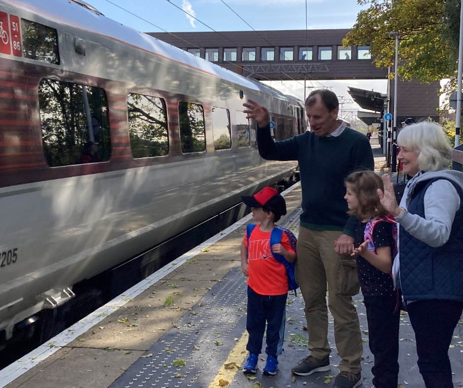 Family on platform waving at train as it pulls into station