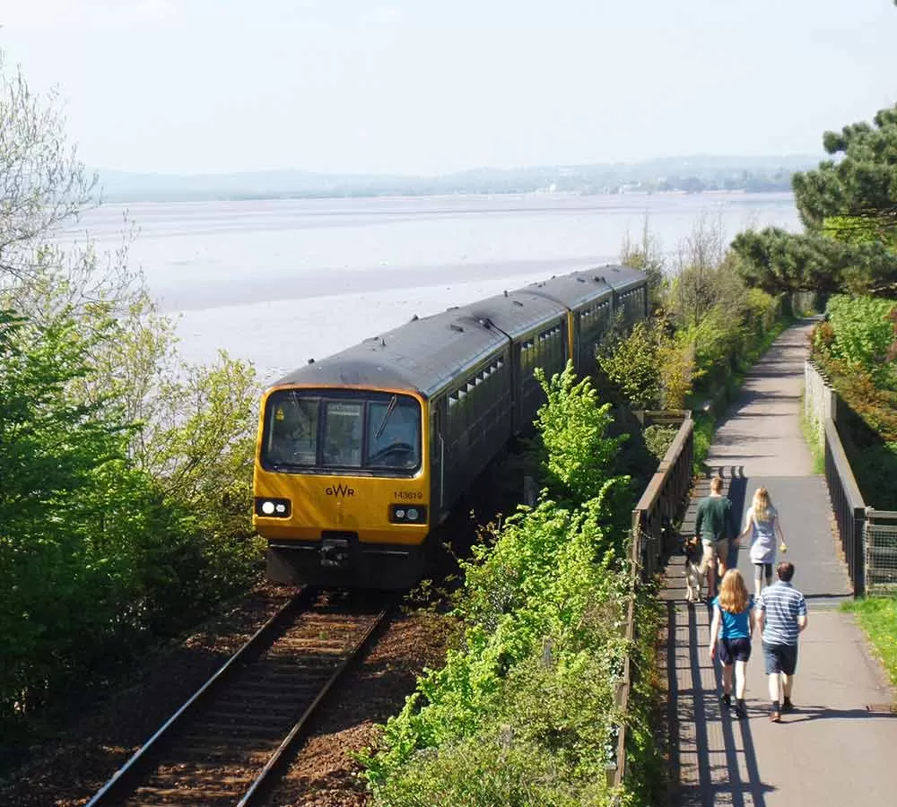 Train travelling along Avocet Line with people walking at the side