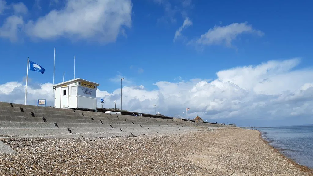 Pebbled beach with blue flag flying on a sunny day | Swale Line