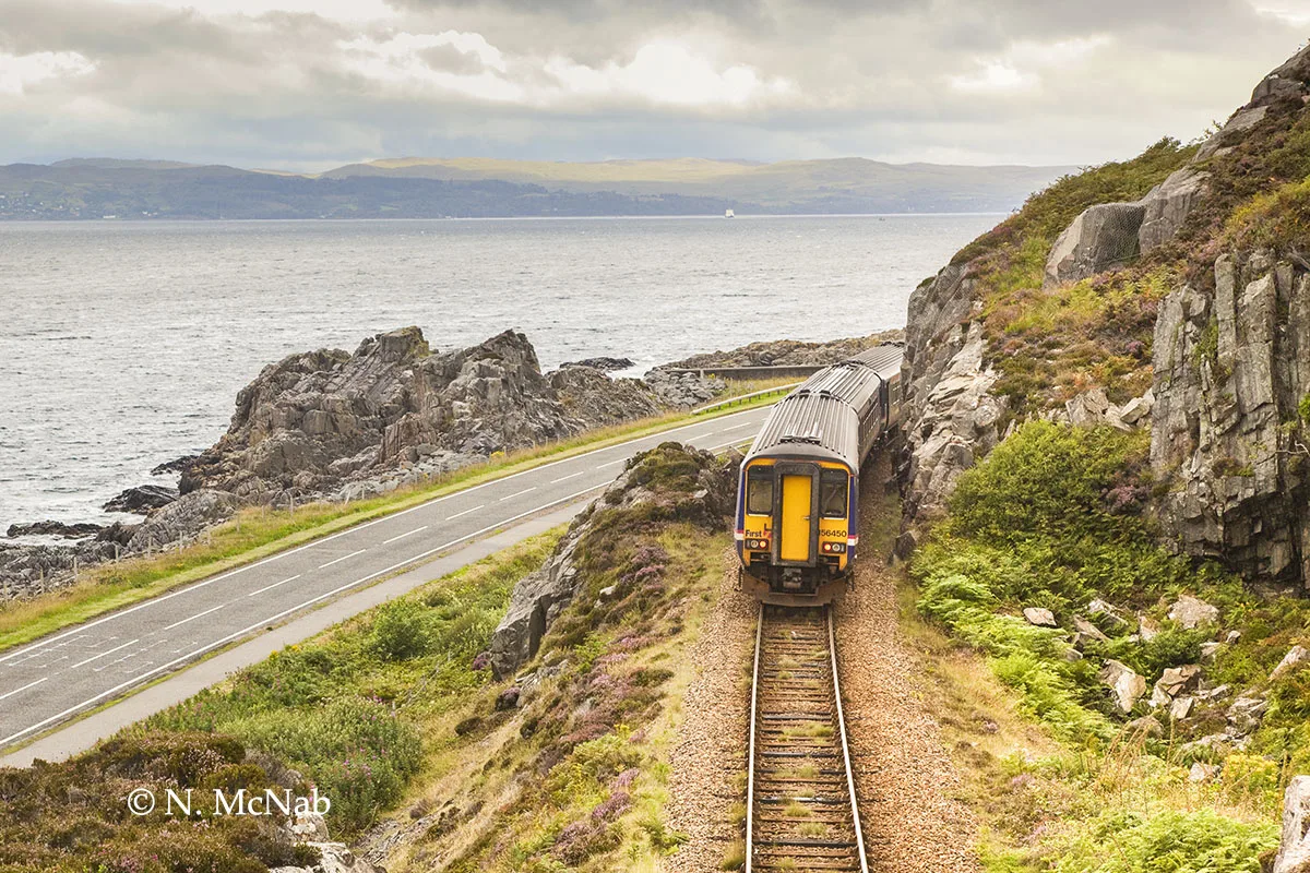 Train travelling by the coast with the road inbetween - top coastal rail routes for seaside views