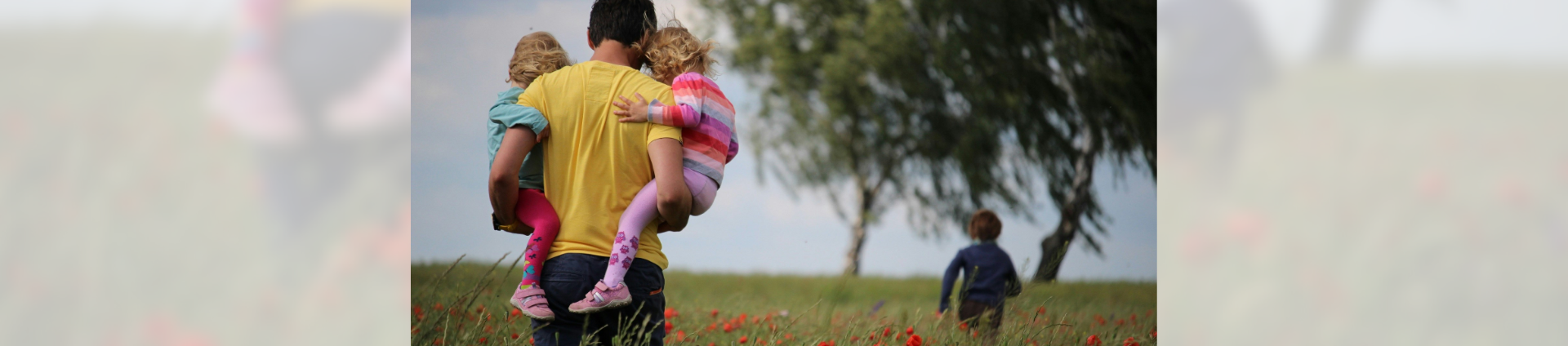 Person holding children in each arm with a child running in the background through poppy fields - great days out with good journey