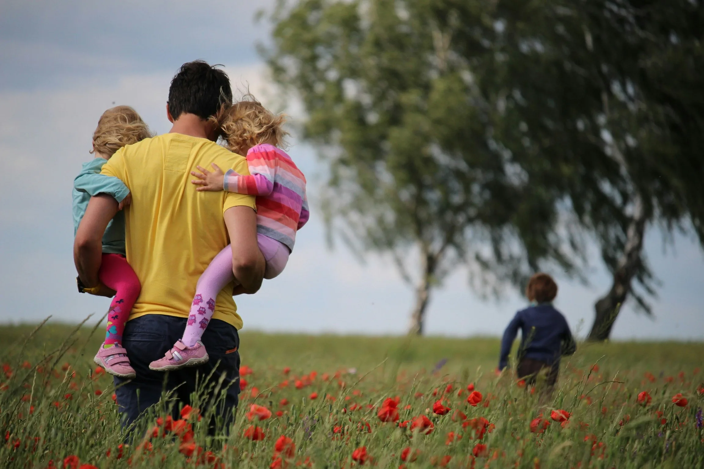 Person holding children in each arm with a child running in the background through poppy fields - great days out with good journey