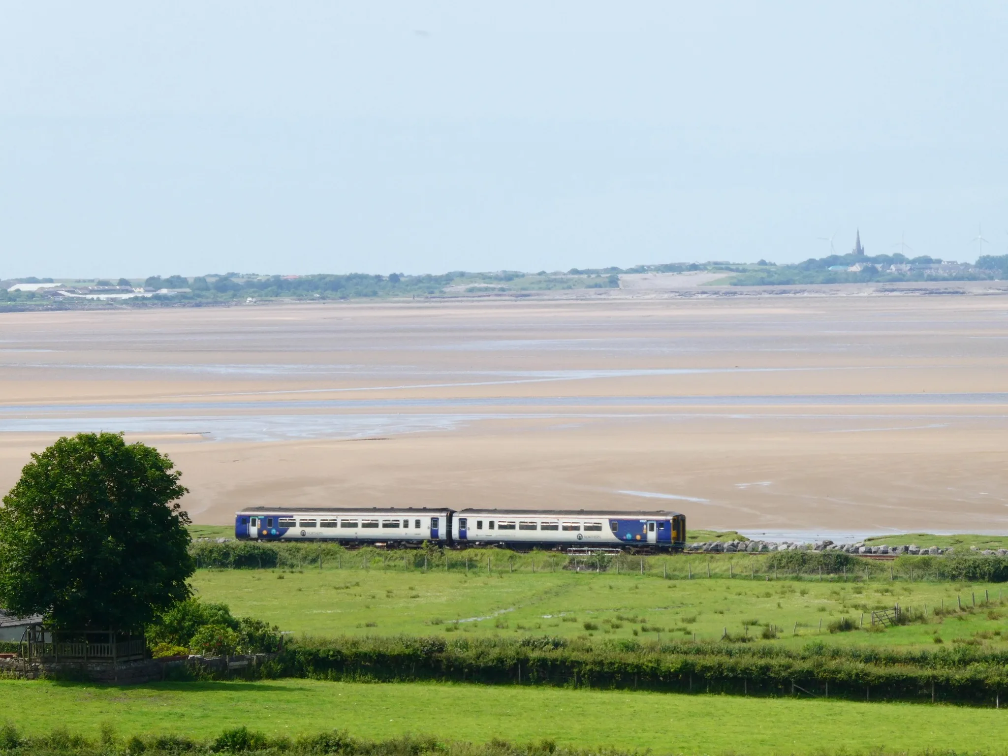 Train travelling along side of estuary with sand and a view beyond of Millom