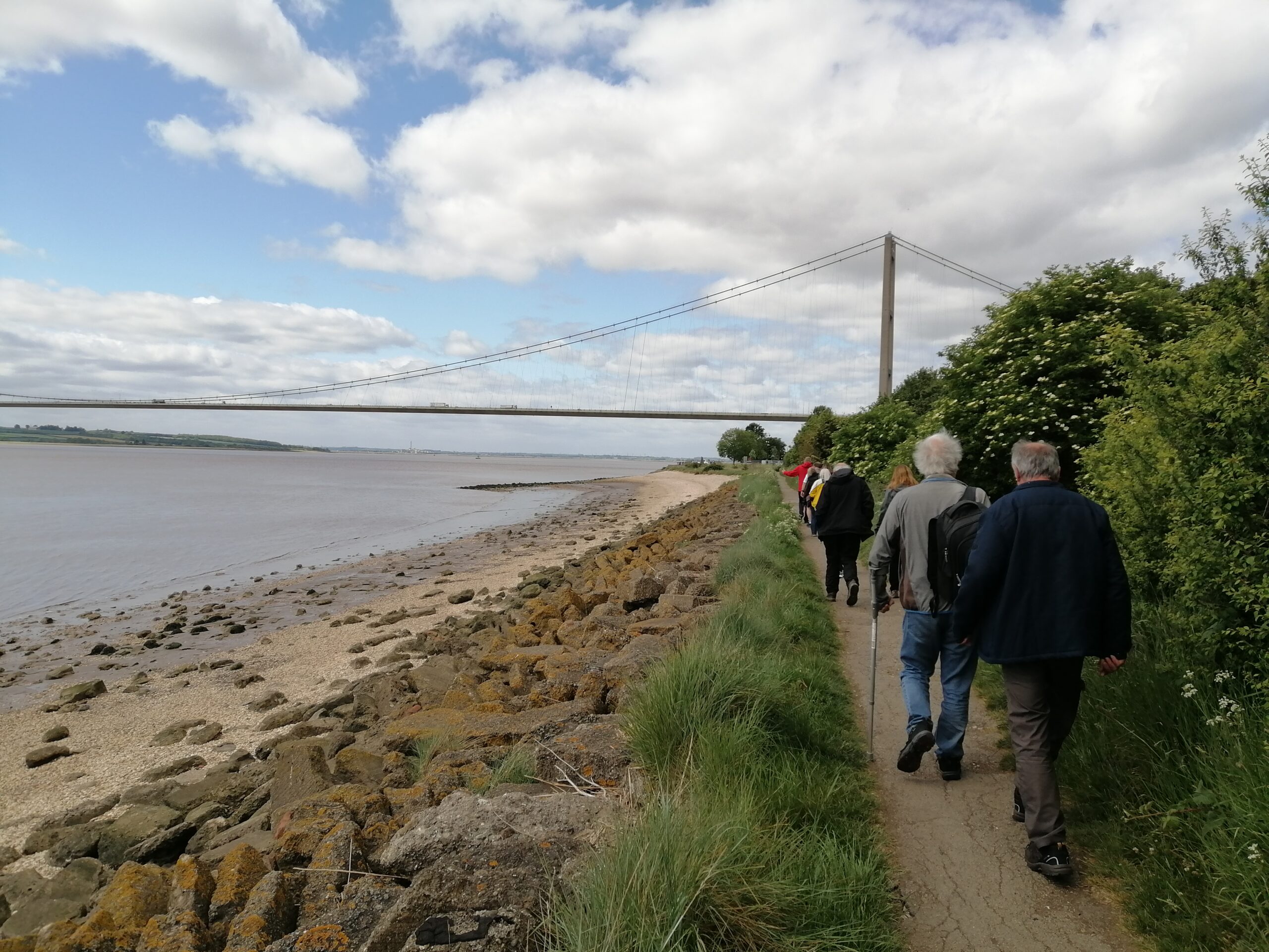 People walking at the side of the estuary with the tall suspension bridge in the background. Along the Yorkshire Coast Line | Summer days out by train for less.