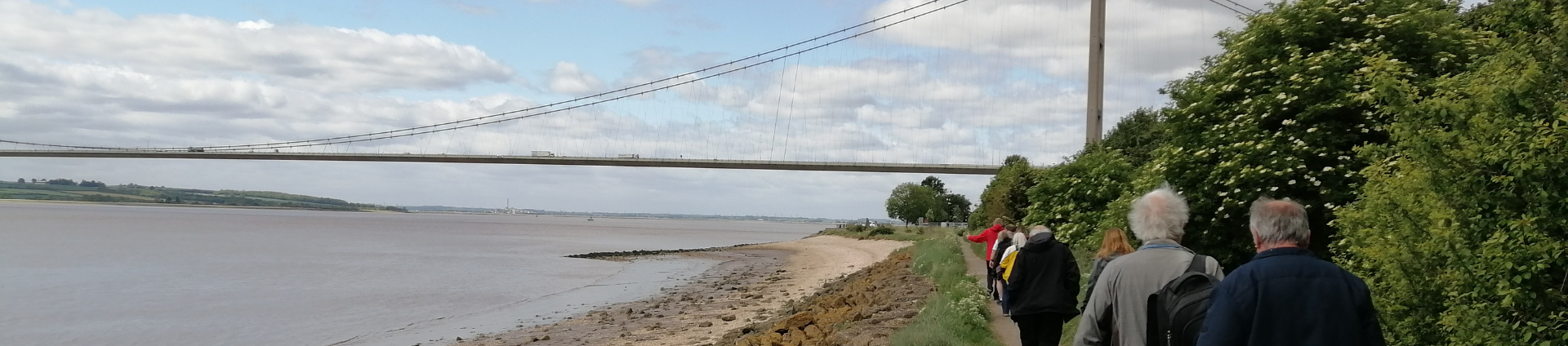 People walking at the side of the estuary with the tall suspension bridge in the background. Along the Yorkshire Coast Line.
