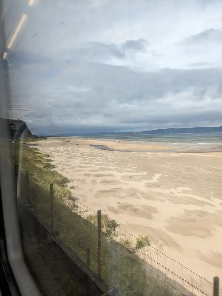 View from the train window of golden sandy beach and mountains in the background. A small sliver of water can be seen between the sand and mountains. #scenicrailview