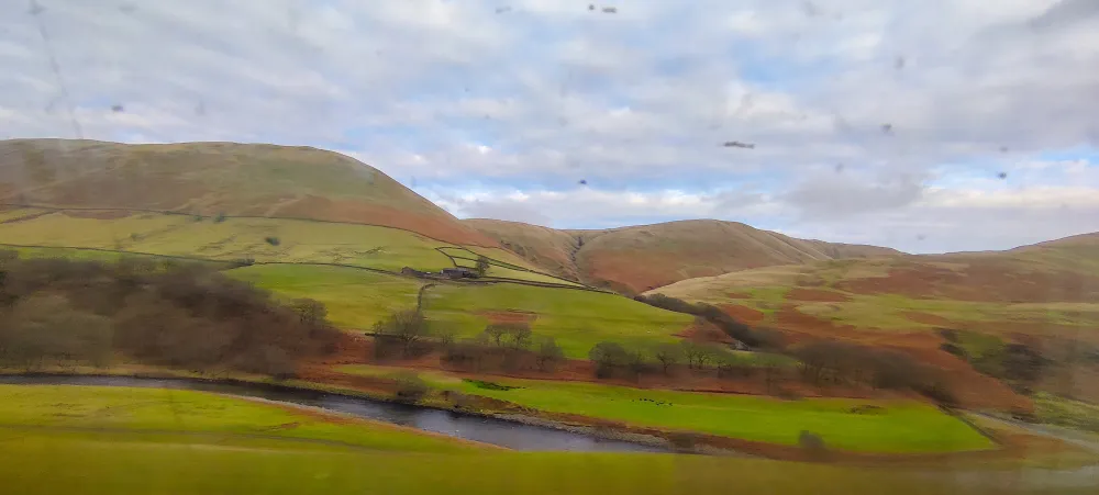 Rolling hills with autumnal shades of orange and brown, the sun hides behind fluffy clouds and peeking blue sky #scenicrailview