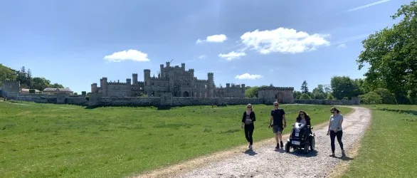 Mobility scooter stood alongside people on a walk around Lowther Castle with the stone ruins in the background.