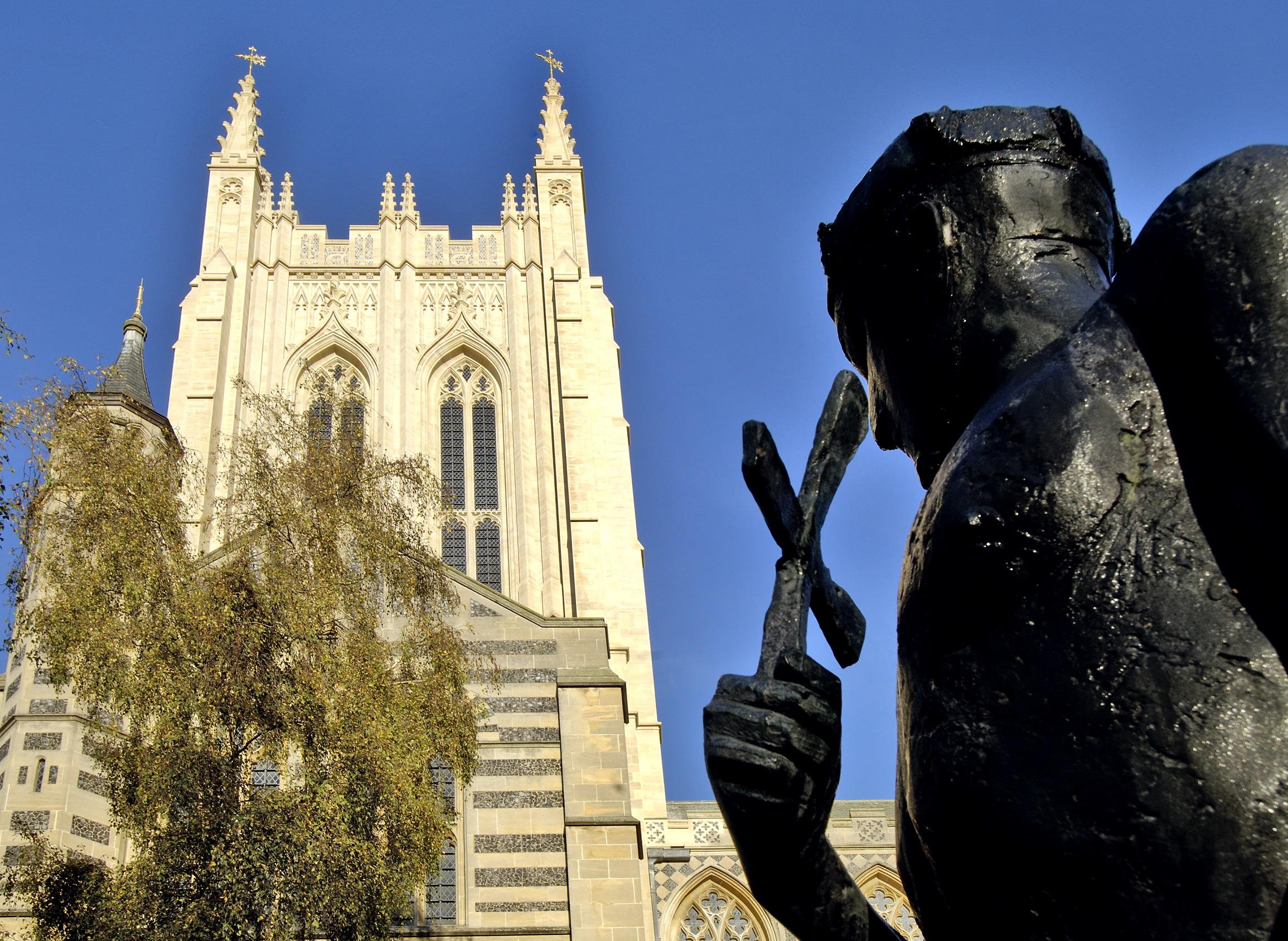 View of a cathedral spire with a statue in the foreground against a blue sky background. St. Edmund's Line