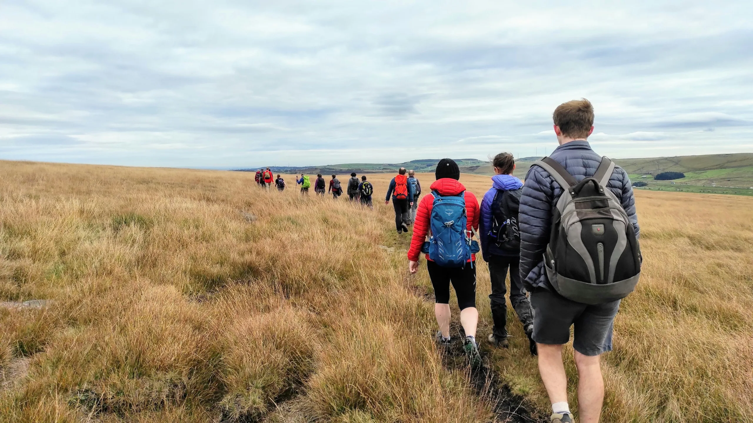Group of people in a line walking through grassland with rolling hills in the background. Beyond the City - exploring greater manchester by train