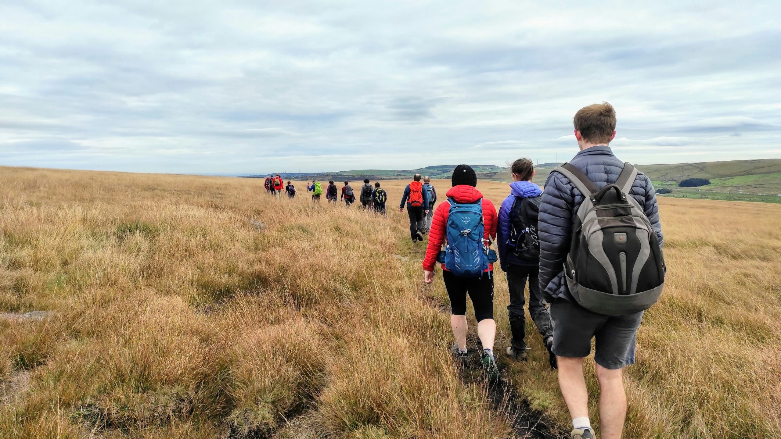 Group of people in a line walking through grassland with rolling hills in the background. Beyond the City - exploring greater manchester by train