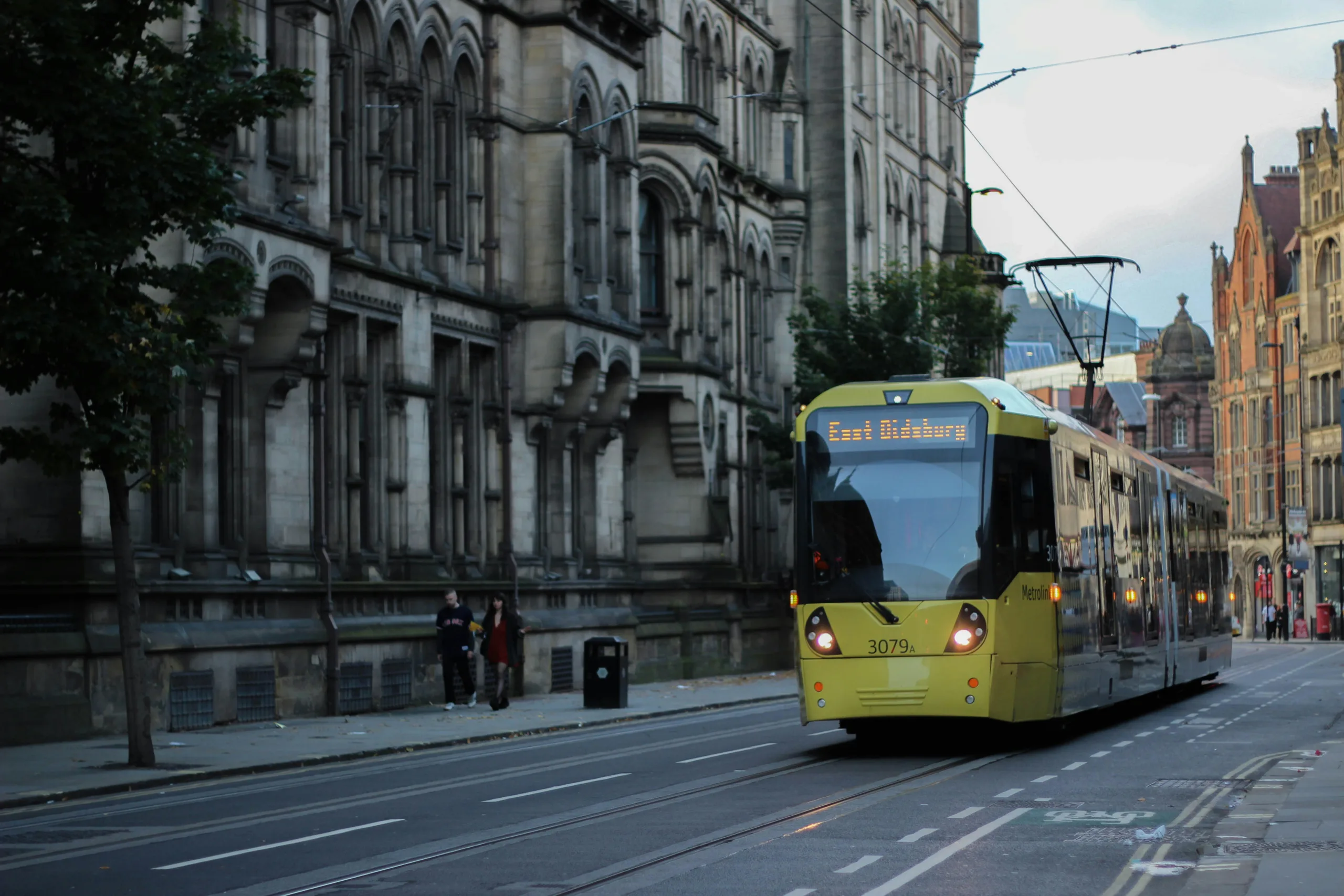 View of a yellow tram coming towards the camera with a historic building on the left.